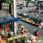 People eating at a street food stall beside a fruit market in Hanoi