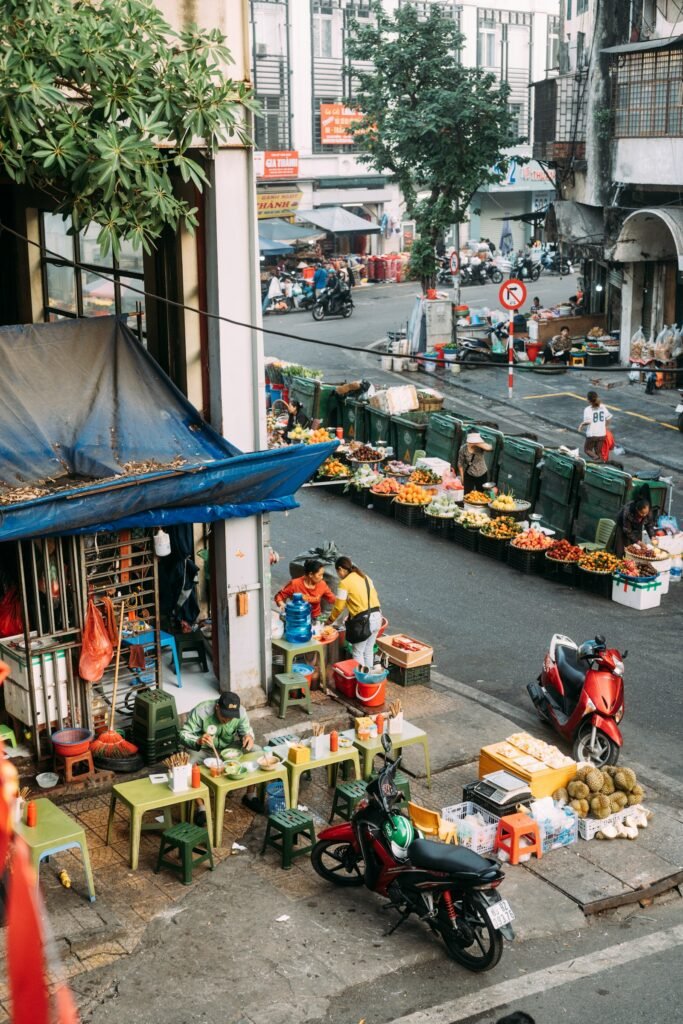 People eating at a street food stall beside a fruit market in Hanoi