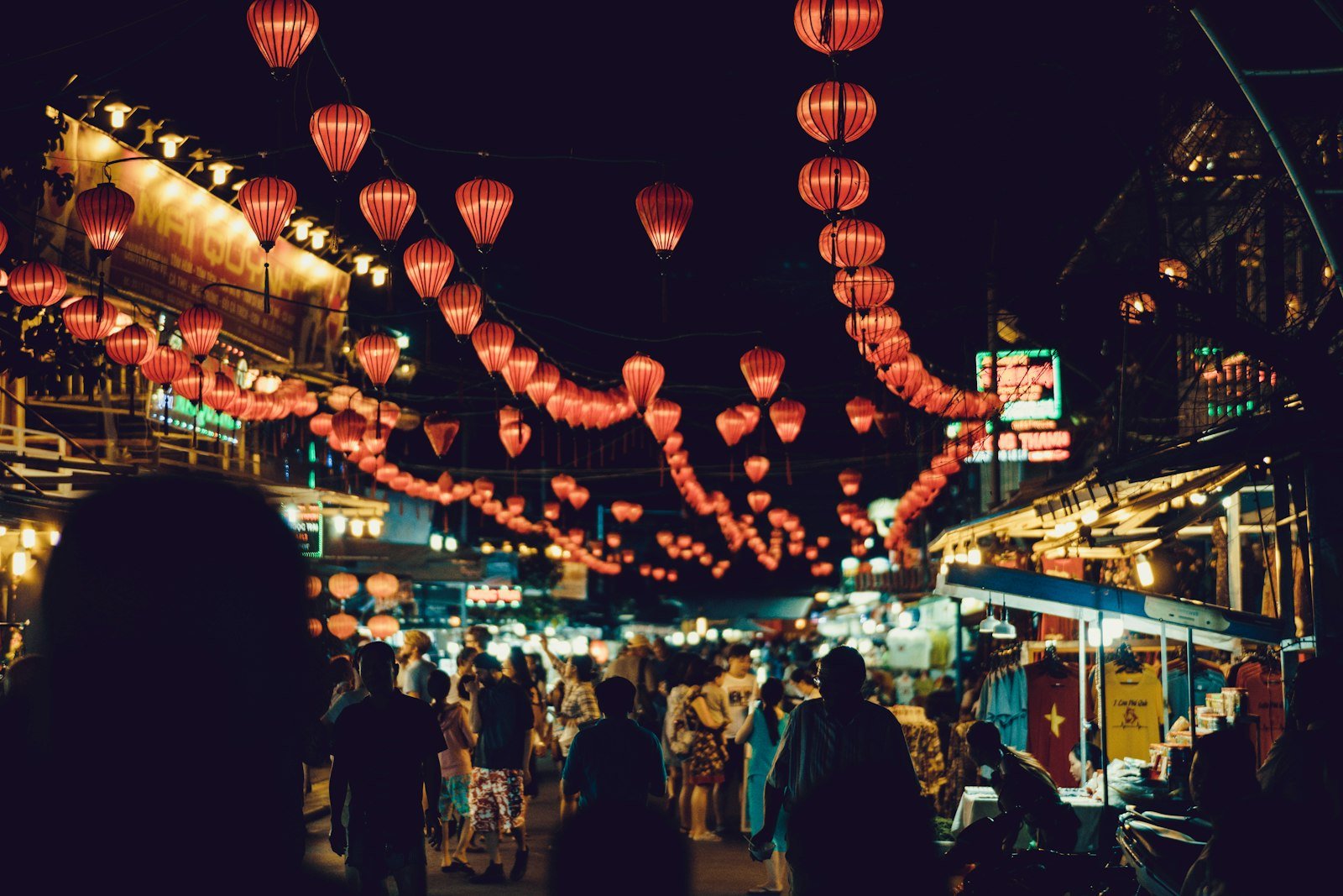 People walking between food stalls under lanterns in Hoi An