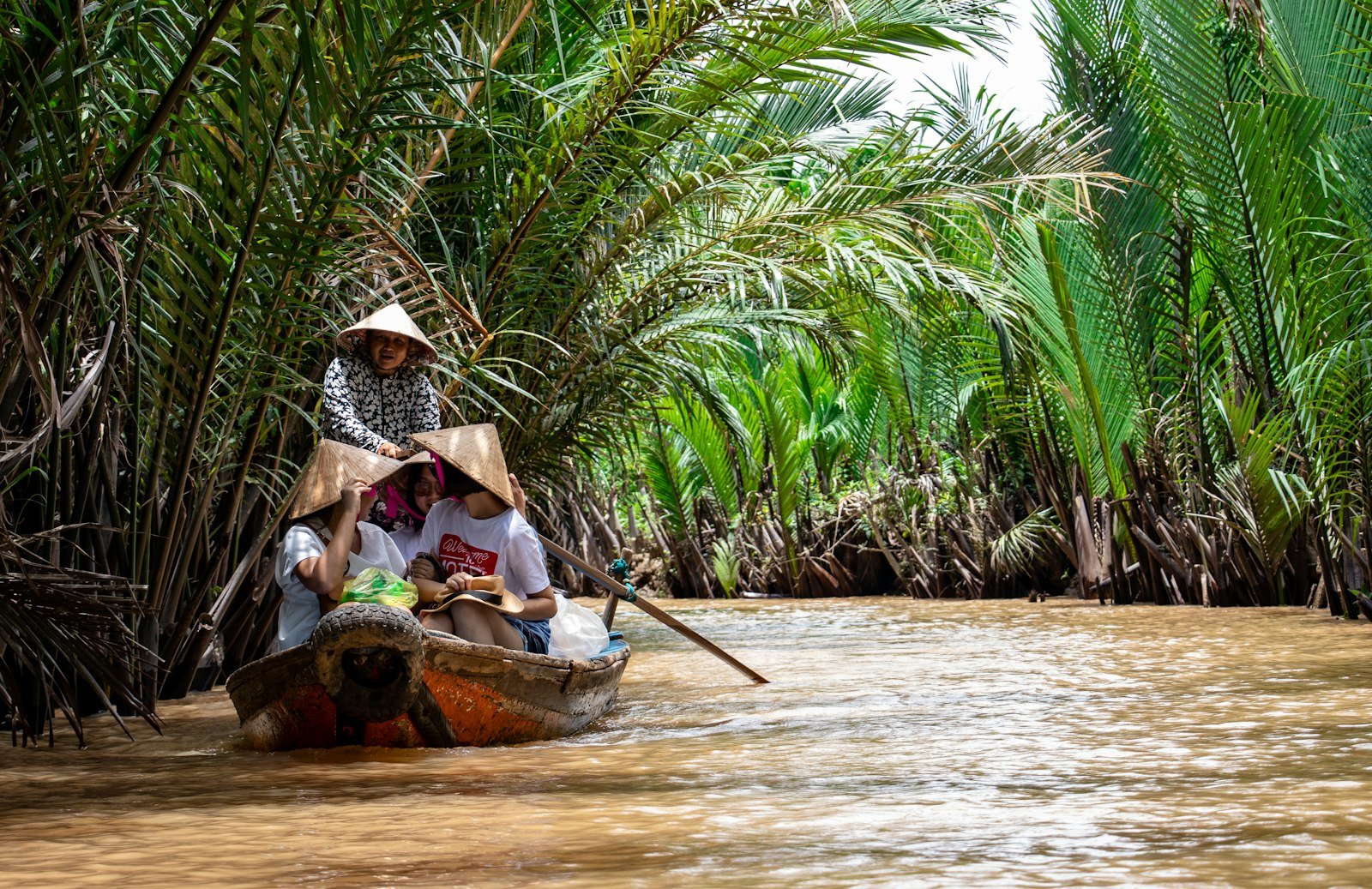 People riding a small canoe on a canal in the Mekong Delta