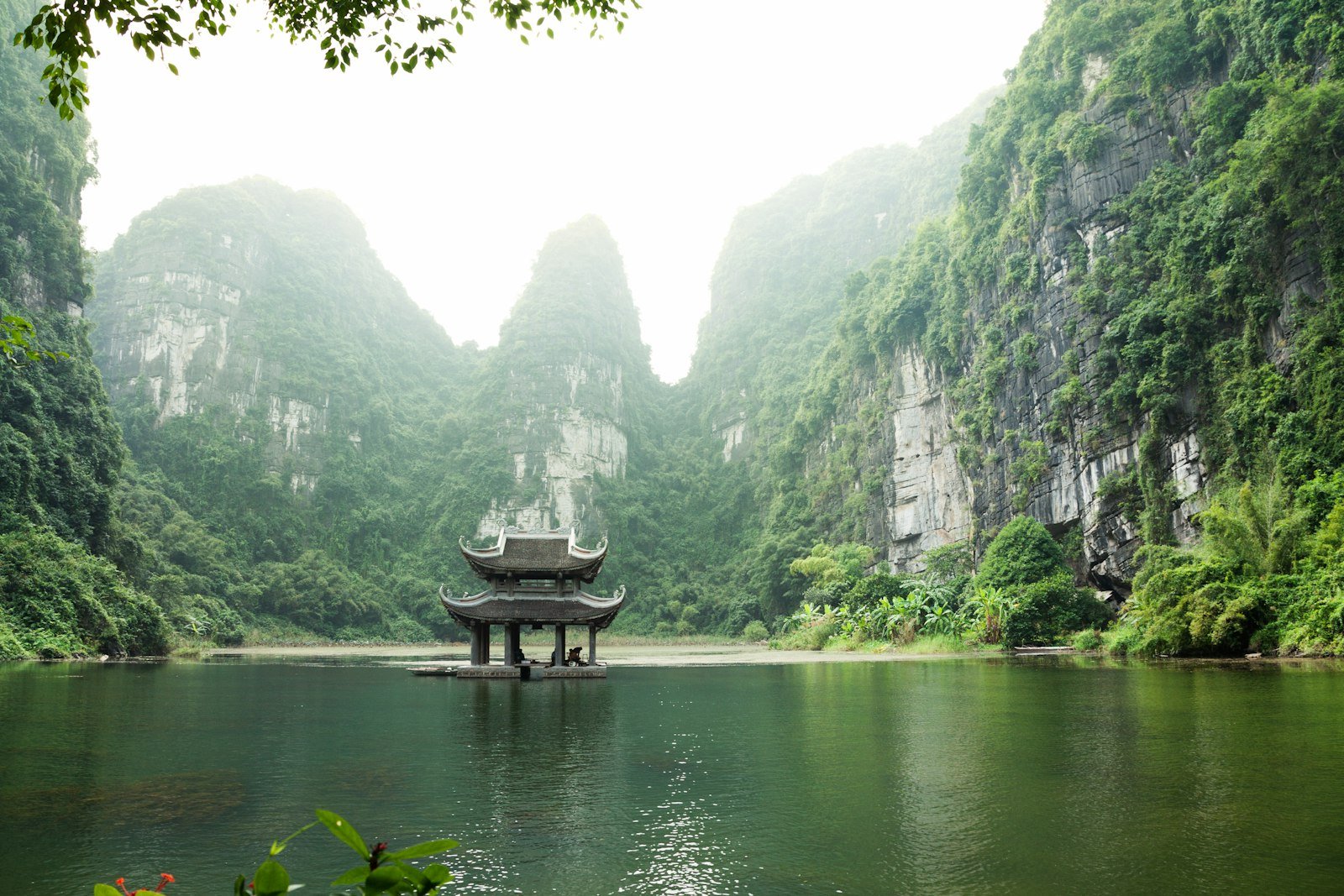 A pagoda by the water surrounded by limestone mountains in Ninh Binh