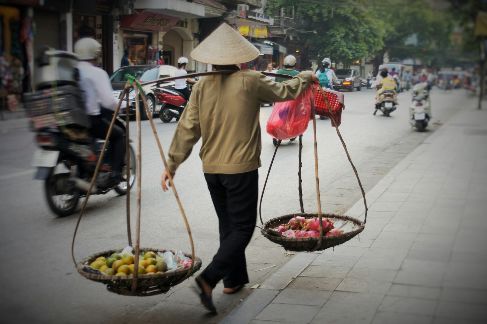 A street vendor carrying two baskets of fruit on a shoulder pole